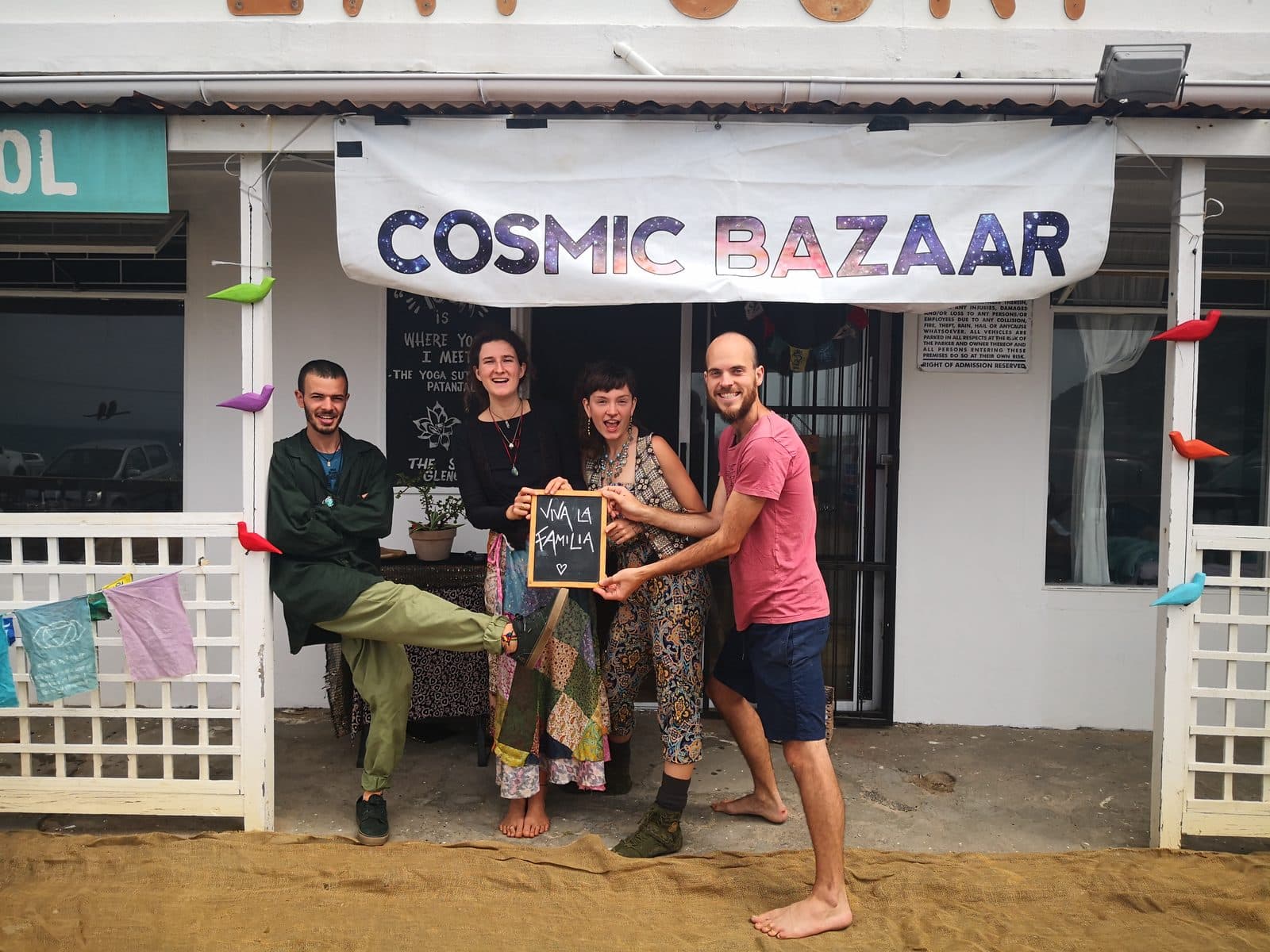 The crew outside the Glencairn shop under the hand-painted Cosmic Bazaar banner, holding a Viva la Familia chalkboard.